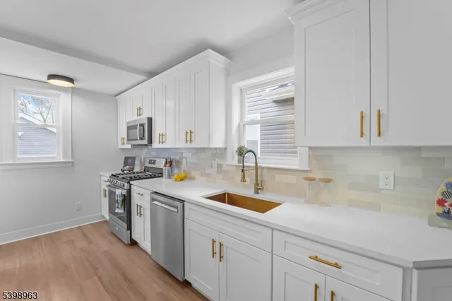 a kitchen with a sink dishwasher a stove and white cabinets with wooden floor