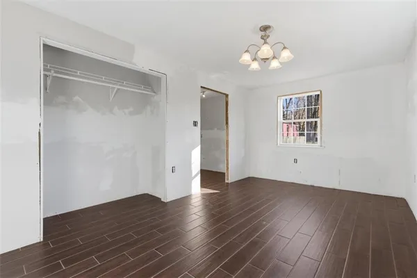 an empty room with wooden floor chandelier and windows