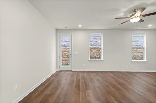 an empty room with wooden floor chandelier fan and windows