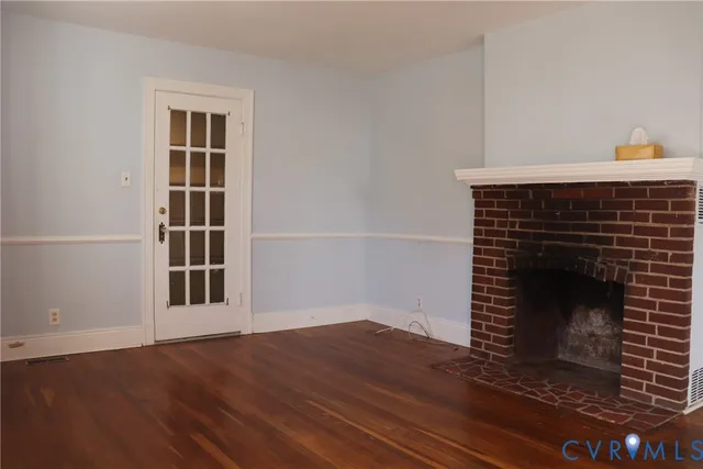 a view of an empty room with wooden floor and a fireplace