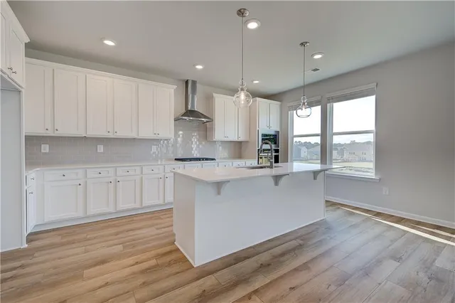 a large kitchen with stainless steel appliances granite countertop a stove a sink and white cabinets with wooden floor