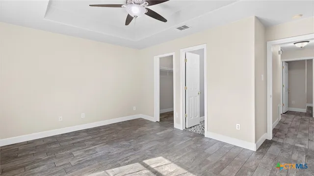 an empty room with wooden floor fan and windows