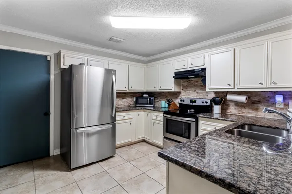 a kitchen with granite countertop a refrigerator a sink a stove top oven and cabinets