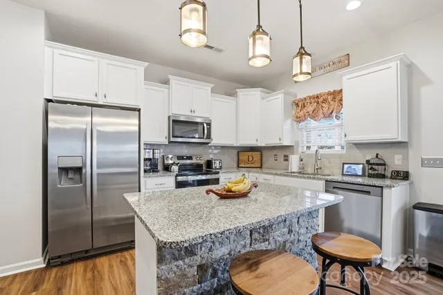 a kitchen with stainless steel appliances granite countertop a sink a stove a refrigerator cabinets and chairs