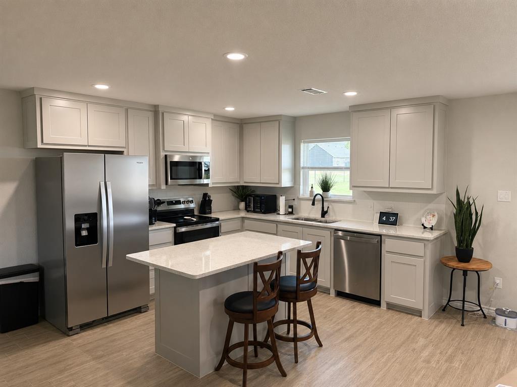 2998 Knob Road Springtown, TX 76082 - Photo 3 of 12 Modern kitchen featuring light gray cabinetry, stainless steel appliances, a center island with countertop seating, recessed lighting.