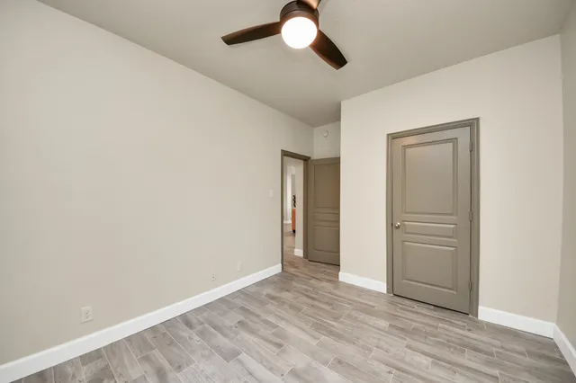 an empty room with wooden floor chandelier fan and windows
