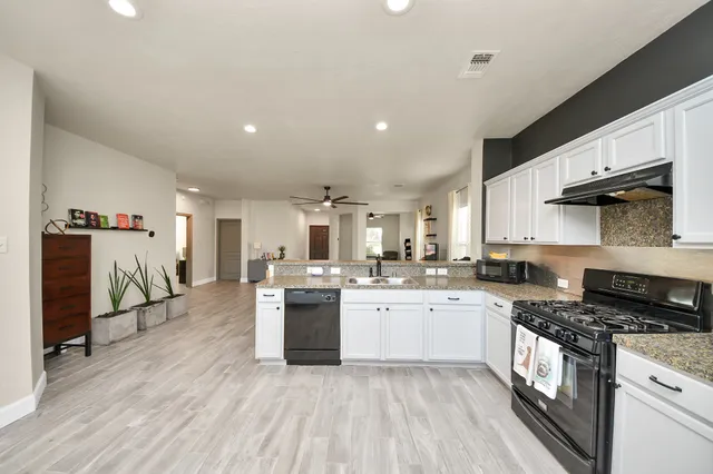 a kitchen with stainless steel appliances granite countertop a stove top oven a sink a dining table and chairs with wooden floor