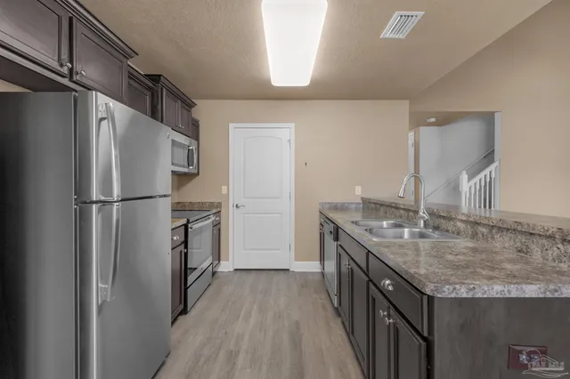 a kitchen with stainless steel appliances granite countertop a refrigerator a sink dishwasher a stove and white countertops with wooden floor