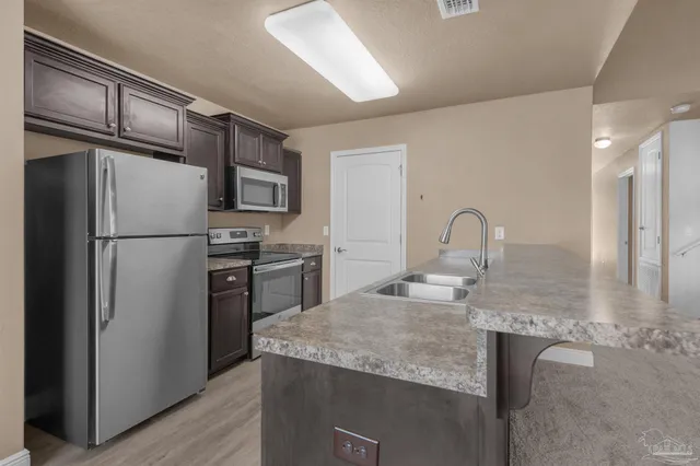 a kitchen with stainless steel appliances granite countertop a refrigerator a stove and a sink with wooden floor