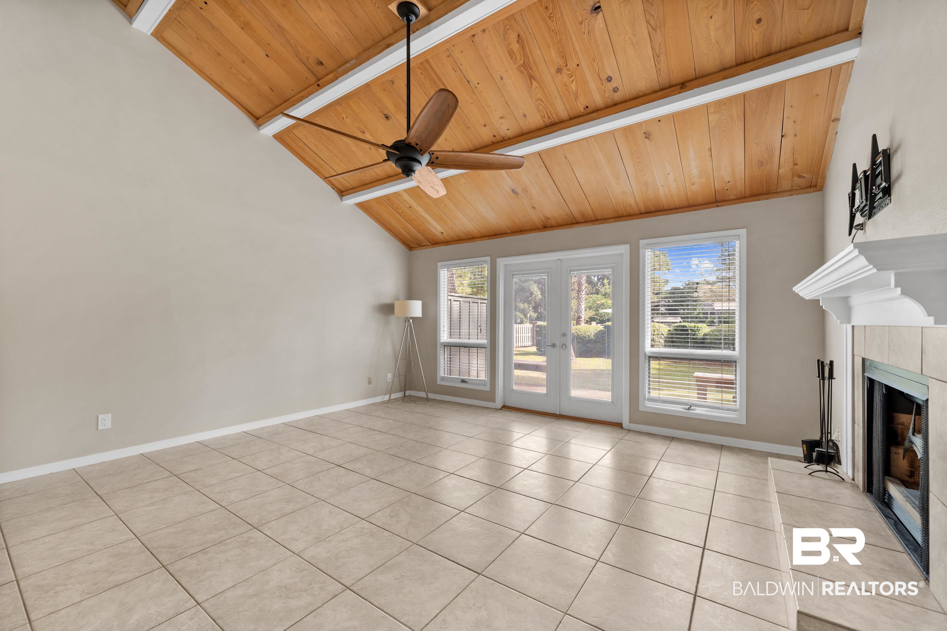 1701 Regency Road, Unit 111 Gulf Shores, AL 36542 - Photo 7 of 29 Unfurnished living room with wood ceiling, light tile patterned floors, ceiling fan, a fireplace, and french doors