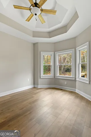 an empty room with wooden floor chandelier fan and windows