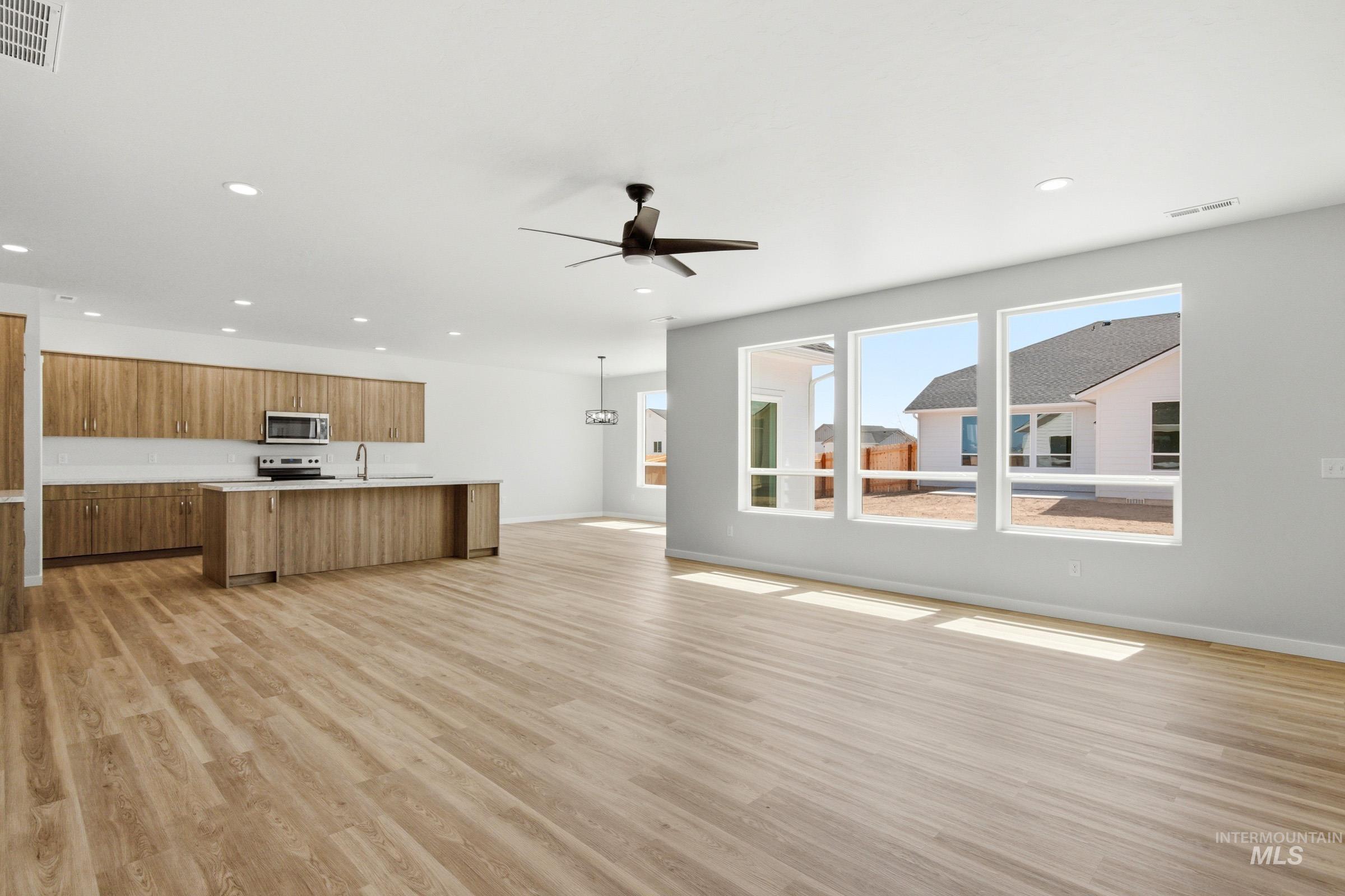 13649 Inman Court Caldwell, ID 83607 - Photo 11 of 22 Open-concept living area featuring wood-finish flooring, a kitchen island with a single-basin sink, wood-finish cabinetry, a white tile backsplash, and stainless steel appliances including a microwave and range