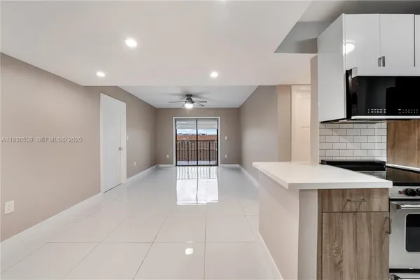 a view of an empty room with kitchen and window