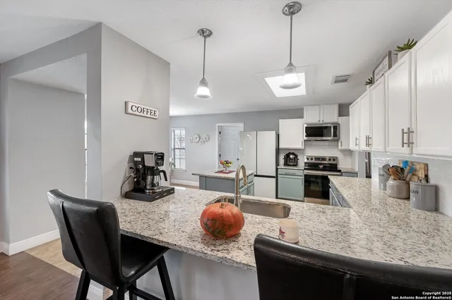 a kitchen with stainless steel appliances granite countertop a sink a stove and chairs with wooden floor