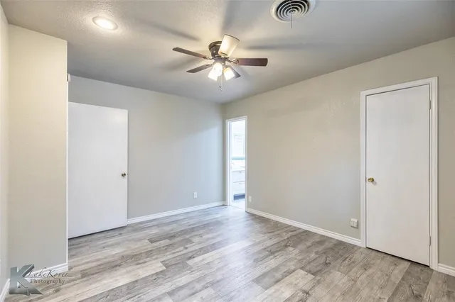 an empty room with wooden floor fan and windows