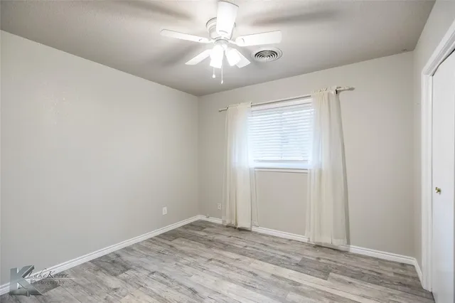 an empty room with wooden floor fan and windows