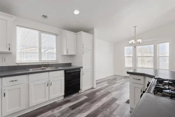 a kitchen with granite countertop a stove a sink and white cabinets with wooden floor