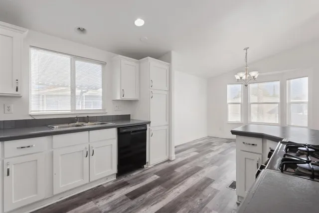 a kitchen with granite countertop a stove a sink and white cabinets with wooden floor