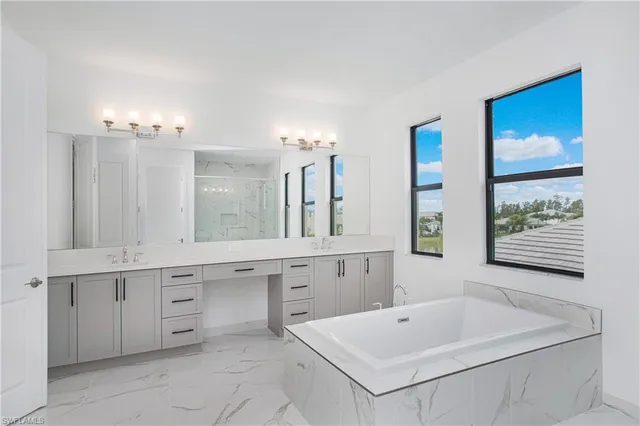 a bathroom with a bathtub a double vanity sink a window and a mirror