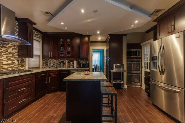 a kitchen with stainless steel appliances granite countertop a refrigerator a sink dishwasher a stove with wooden cabinets and floor