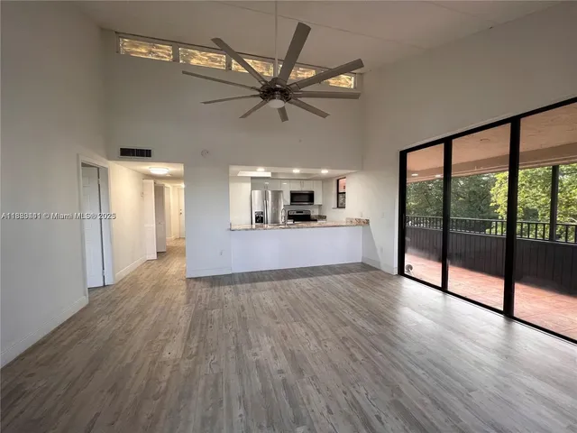 a view of a big room with wooden floor windows and ceiling fan
