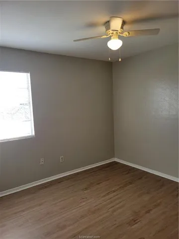 an empty room with wooden floor chandelier fan and windows