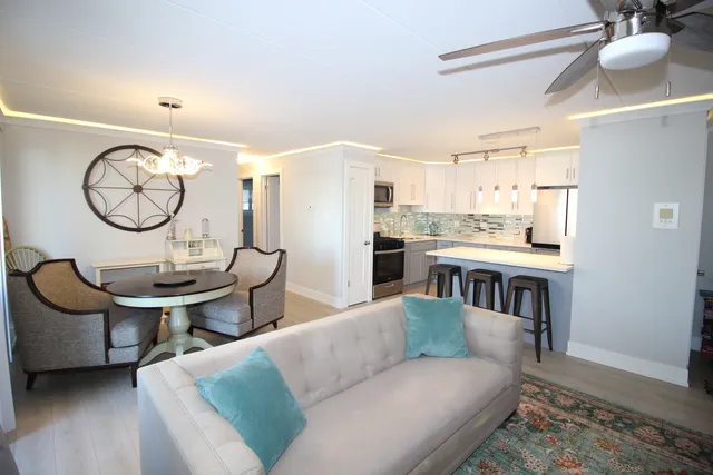 a living room with stainless steel appliances furniture a rug and a kitchen