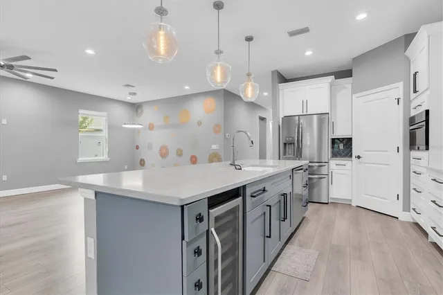 a kitchen with stainless steel appliances kitchen island granite countertop a stove a sink a refrigerator and white cabinets with wooden floor