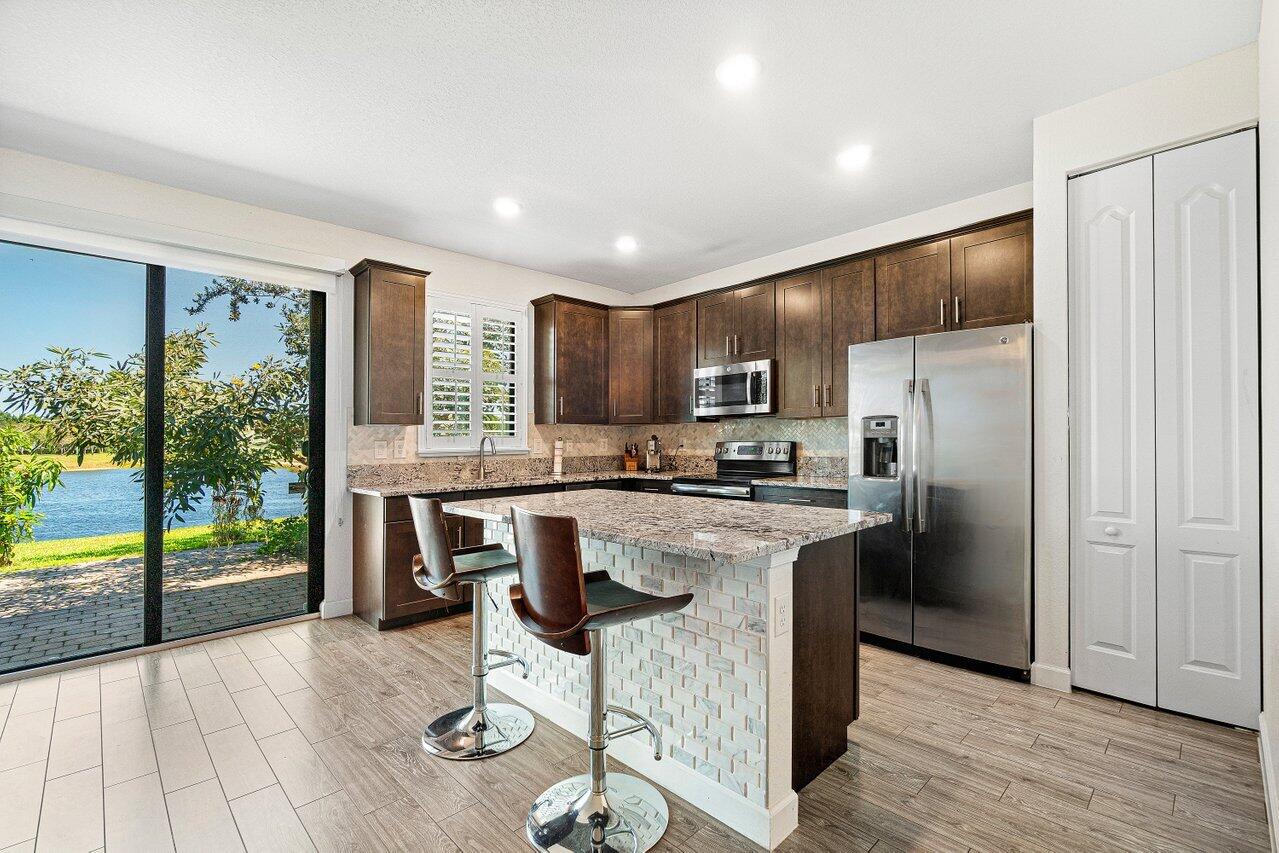 12949 Anthorne Lane Boynton Beach, FL 33436 - Photo 12 of 37 a kitchen with kitchen island wooden cabinets a refrigerator oven a sink and a large window