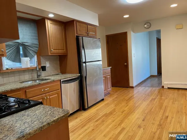 a kitchen with stainless steel appliances granite countertop a refrigerator a sink dishwasher and wooden cabinets with wooden floor