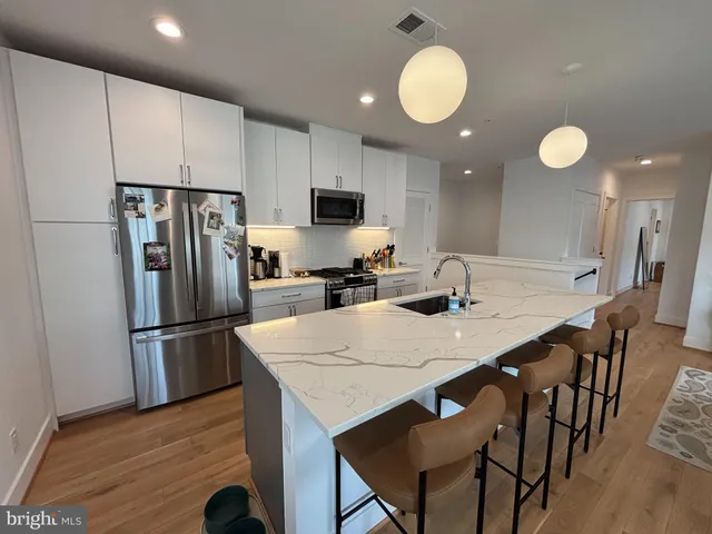 a kitchen with stainless steel appliances granite countertop a refrigerator a stove a sink a dining table and chairs with wooden floor