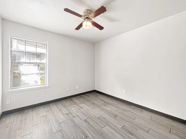 an empty room with wooden floor ceiling fan and windows