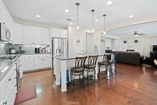 a kitchen with stainless steel appliances granite countertop a stove a refrigerator a kitchen island a dining table and chairs with wooden floor