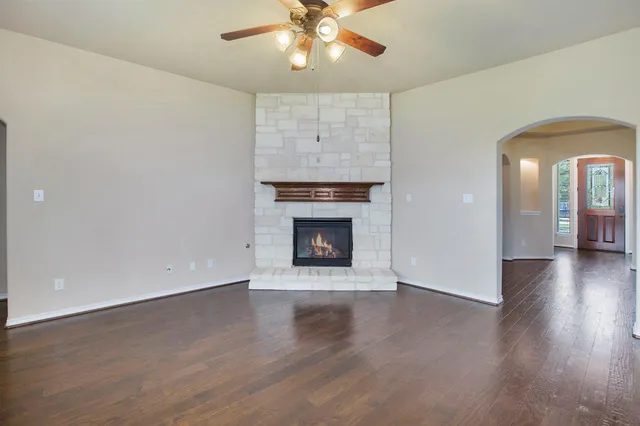 an empty room with wooden floor a chandelier fan and a fireplace