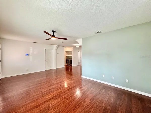 a view of an empty room with wooden floor and a ceiling fan