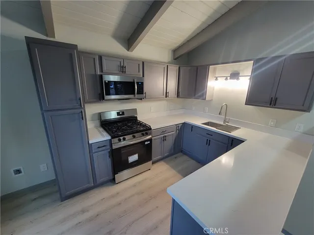 a kitchen with stainless steel appliances a refrigerator a sink a stove a microwave a sink a refrigerator wooden floor and cabinets