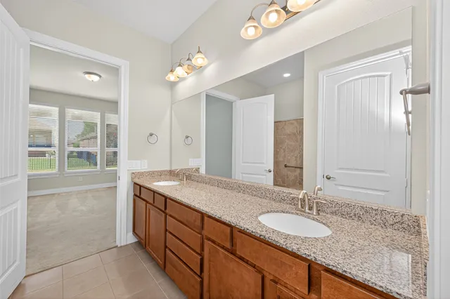 a spacious bathroom with a granite countertop double vanity sink a mirror and a shower