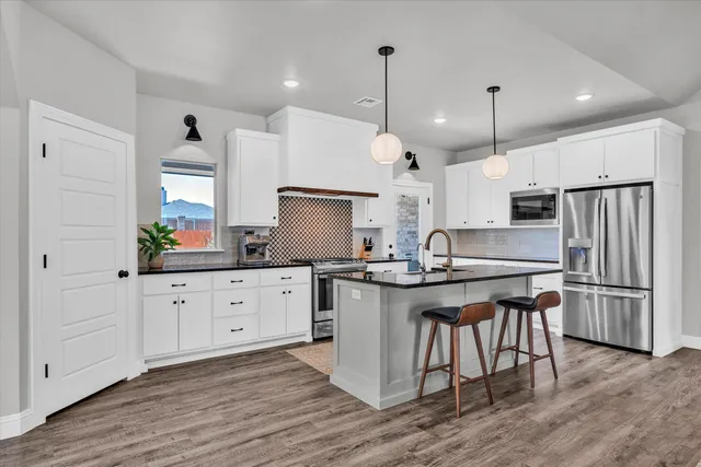 a kitchen with stainless steel appliances granite countertop a sink a stove a refrigerator and white cabinets with wooden floor