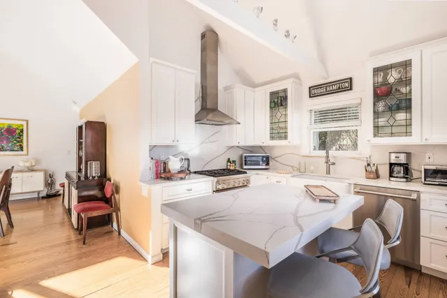 a kitchen with stainless steel appliances a stove a sink a kitchen island with chairs and wooden cabinets