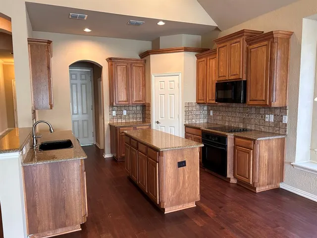 a kitchen with kitchen island granite countertop a stove top oven a sink and dishwasher with wooden floor