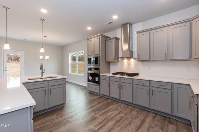 a kitchen with stainless steel appliances kitchen island granite countertop a stove a sink and white cabinets with wooden floor