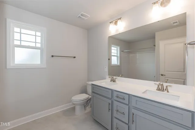 a bathroom with a toilet a sink a mirror a window and vanity