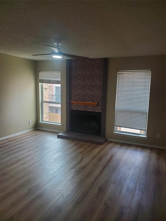 5532 Boca Raton Boulevard, Unit 290 Fort Worth, TX 76112 - Photo 9 of 16 Living area featuring wood-finish flooring, a fireplace with a textured surround and wood mantel, two windows with zebra shades, and a ceiling fan lighting
