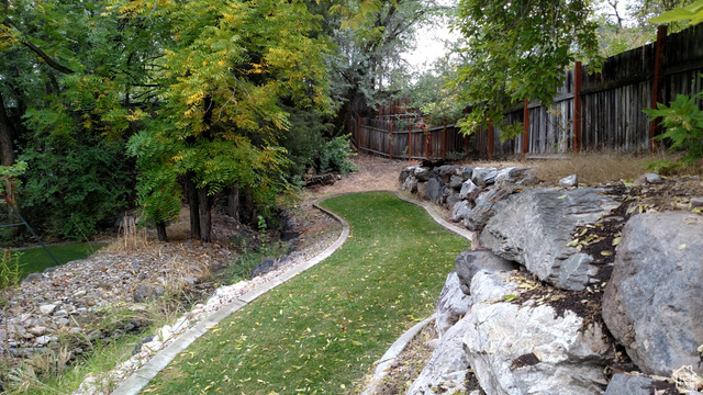 1360 Carterville Road Orem, UT 84097 - Photo 55 of 64 Tiered landscaping with a curved grass pathway, natural rock retaining walls, mature trees, and a wood fence border
