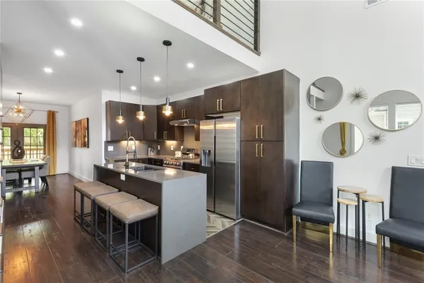 a kitchen with stainless steel appliances granite countertop a refrigerator a stove top oven a dining table and chairs with wooden floor