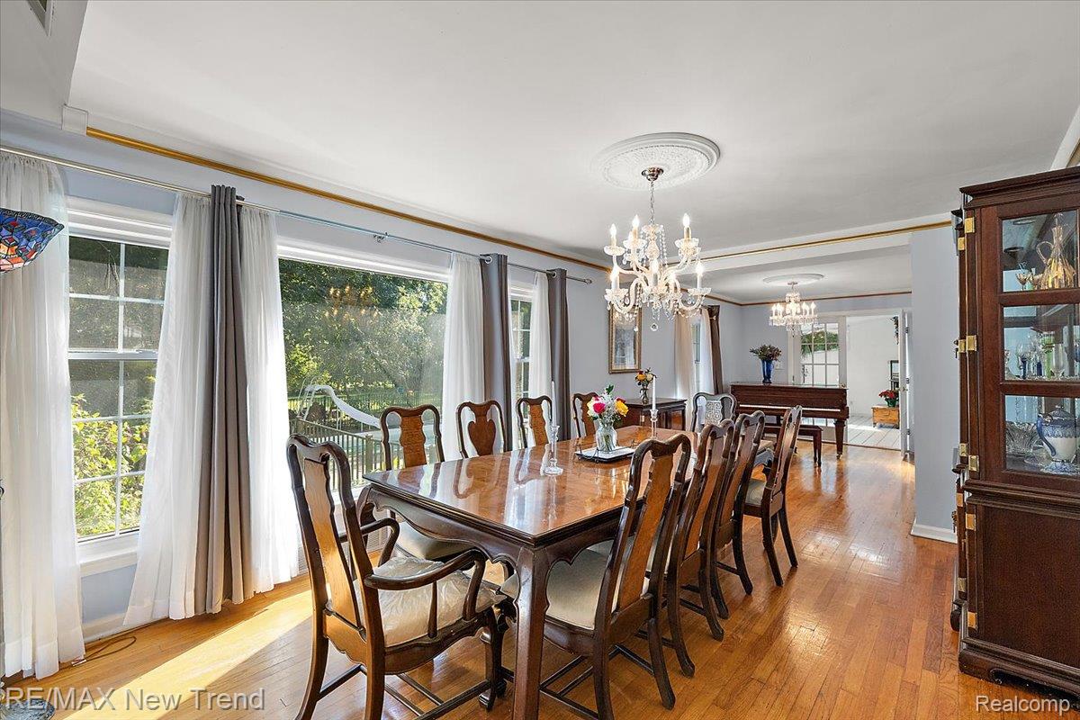 1450 Lenox Road Bloomfield Hills, MI 48304 - Photo 16 of 79 Hardwood flooring throughout, featuring multiple large windows, an elegant chandelier with a ceiling medallion, and a built-in display cabinet
