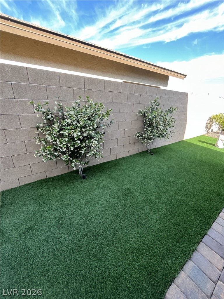 498 Pebble Run Avenue Henderson, NV 89011 - Photo 29 of 47 An immaculately kept private yard featuring lush artificial turf and charming floral plantings along a block fence.