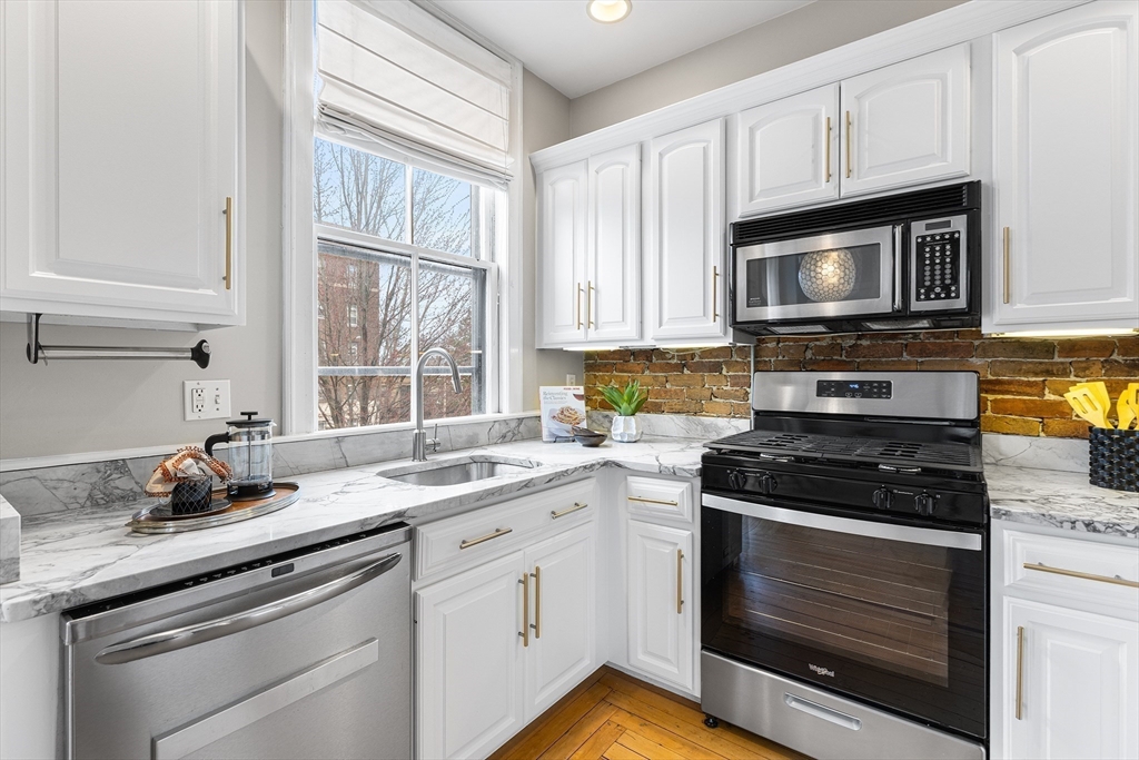 398 Broadway, Unit 2A Somerville, MA 02145 - Photo 8 of 25 a kitchen with granite countertop white cabinets appliances a window and a sink
