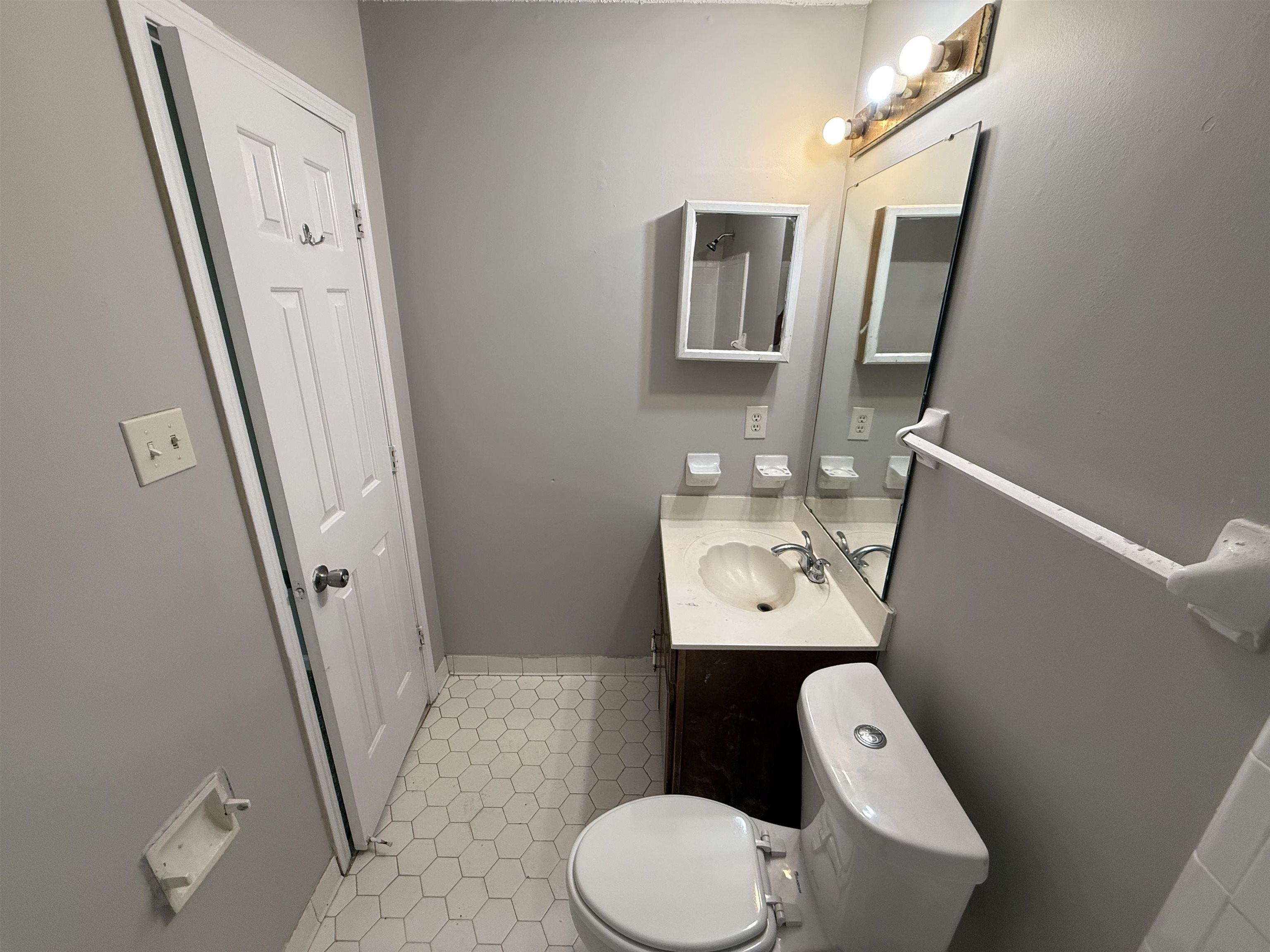 6420 Saginaw Road Memphis, TN 38134 - Photo 30 of 38 Compact bathroom featuring a white hexagonal tile floor, dark wood-finish vanity with a shell-shaped basin, a medicine cabinet, and a wall-mounted mirror