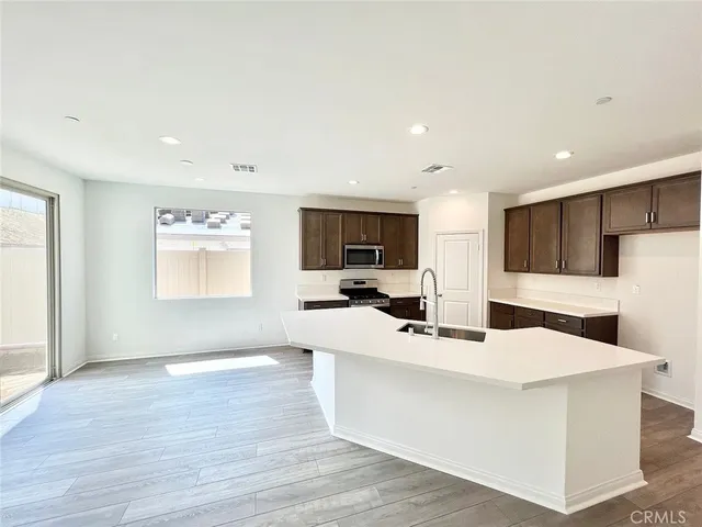 a kitchen with stainless steel appliances a microwave a stove a sink a refrigerator and white cabinets with wooden floor